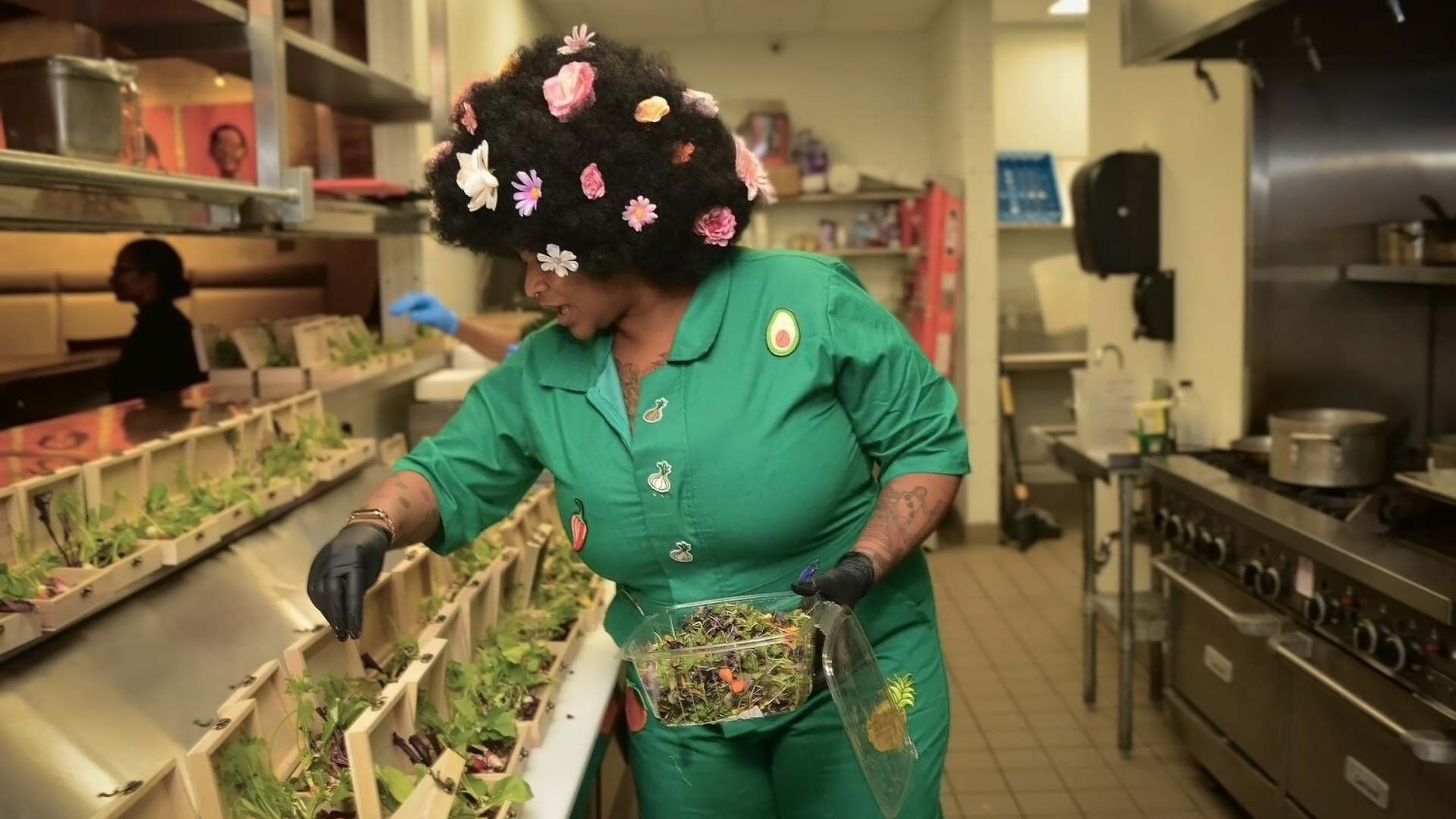 Chef in a green jumpsuit with floral hair styling preparing fresh salads in the Press Street Station kitchen